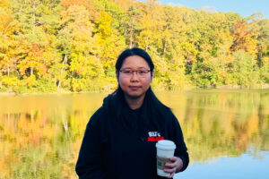 Haoyue Jiang standing in front a lake with fall leaves